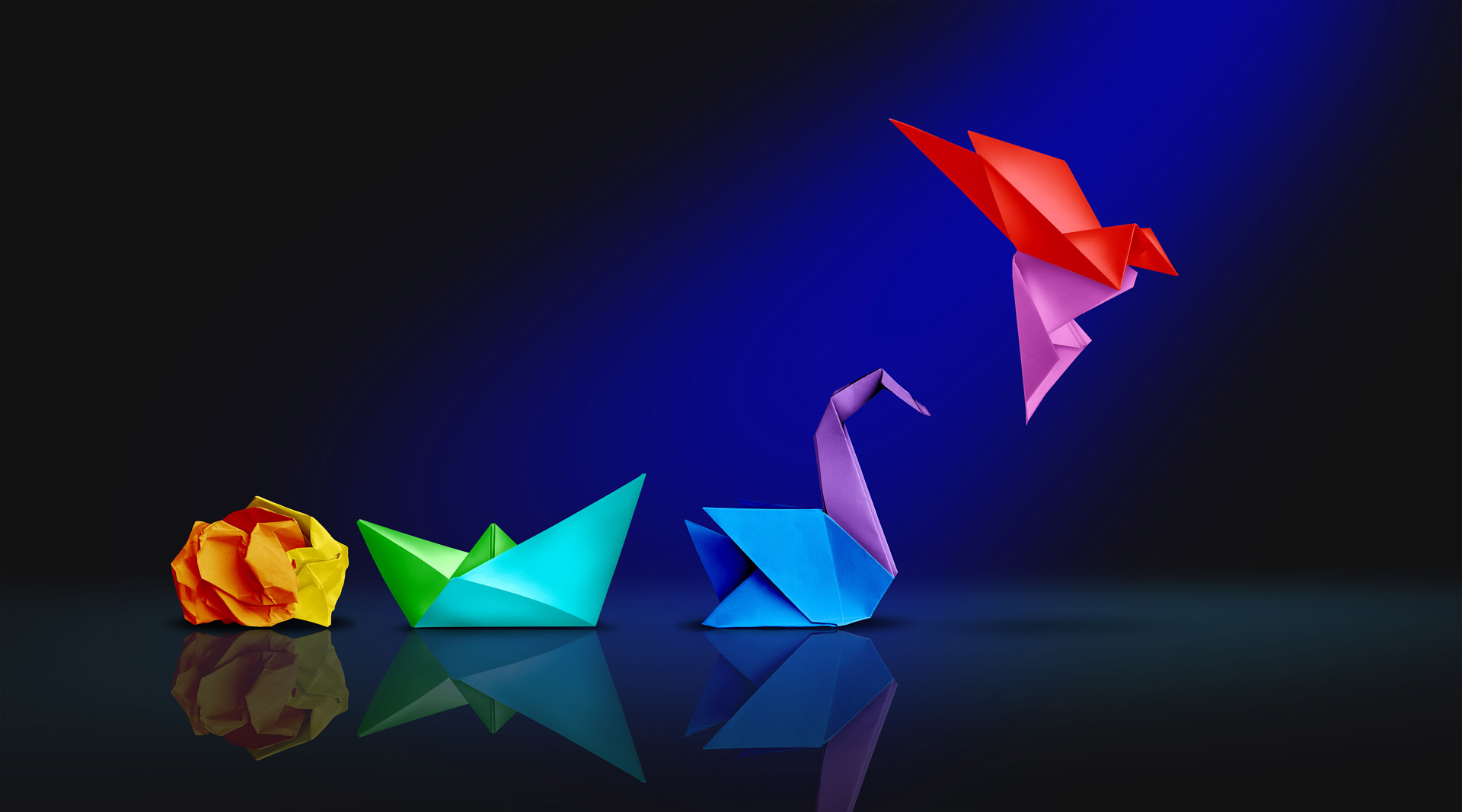 Bunte Origami-Vögel und -Formen Eine Sammlung bunter Origami-Kreationen, darunter eine gelbe zerknüllte Papierform, ein grünes Boot, ein lila Schwan und ein roter und pinker fliegender Vogel, alle vor einem dunkelblauen Hintergrund. Die Papierkreationen reflektieren das Licht und verleihen ihnen ein dynamisches und künstlerisches Aussehen.