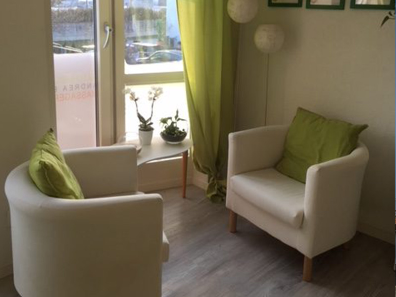 Ein ruhiger und einladender Beratungsraum mit zwei weißen Sesseln, grünen Kissen und sanftem natürlichem Licht, das durch das Fenster strömt. Der Raum hat grüne Vorhänge, einen kleinen Tisch mit Pflanzen und Bilderrahmen an der Wand.